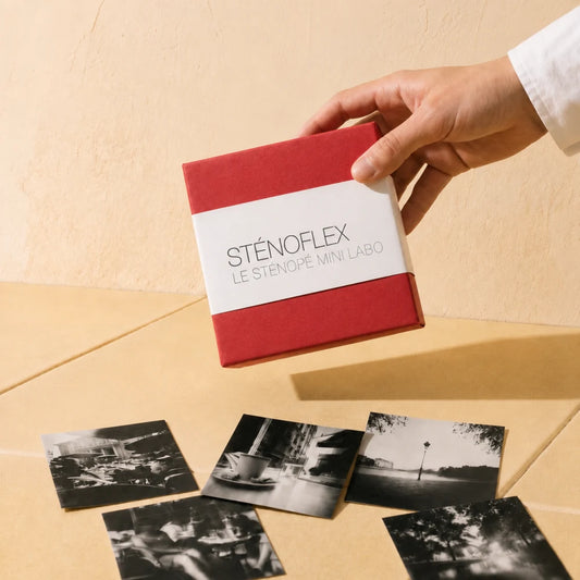 Boîte sténopé Sténoflex rouge tenue à la main au-dessus de tirages noir et blanc
